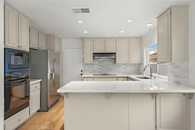 kitchen with black appliances, sink, backsplash, kitchen peninsula, and light wood-type flooring