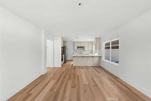 kitchen featuring tasteful backsplash, light wood-type flooring, sink, and stainless steel refrigerator