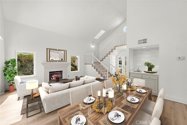 dining room featuring light wood-type flooring, a brick fireplace, a skylight, and high vaulted ceiling