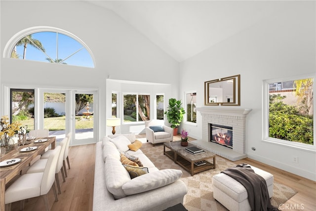 living room featuring light wood-type flooring, a brick fireplace, plenty of natural light, and high vaulted ceiling