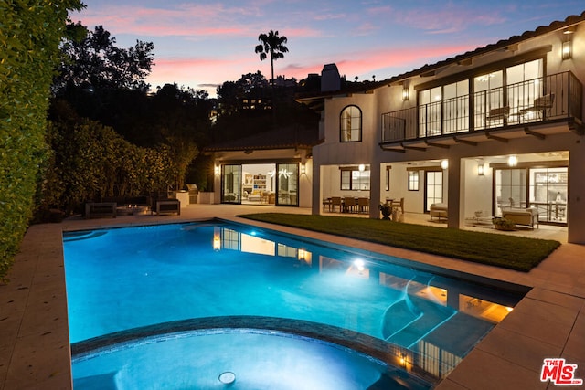 pool at dusk featuring a yard, a patio, and an in ground hot tub