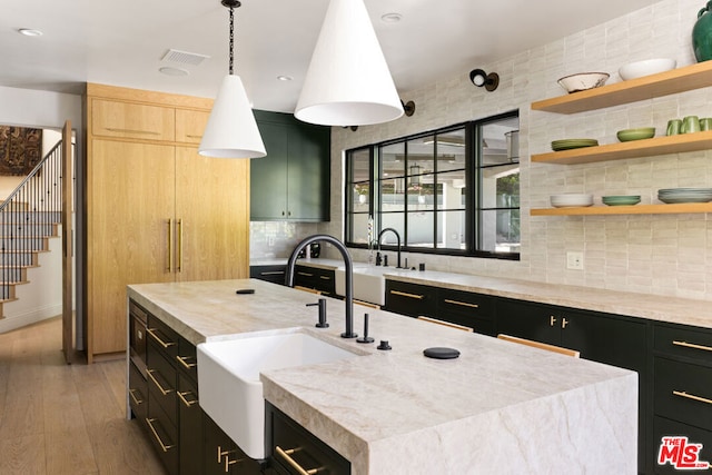 kitchen with hardwood / wood-style flooring, a center island with sink, light brown cabinets, hanging light fixtures, and sink