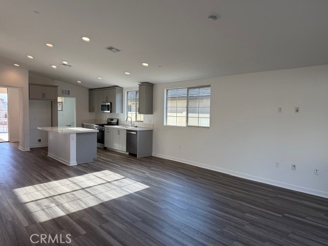 kitchen with a sink, a center island, gray cabinets, appliances with stainless steel finishes, and dark wood-style flooring