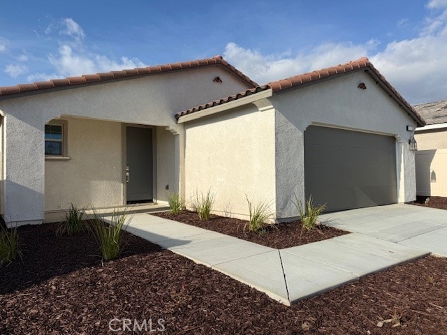 mediterranean / spanish house with a garage, driveway, stucco siding, and a tiled roof