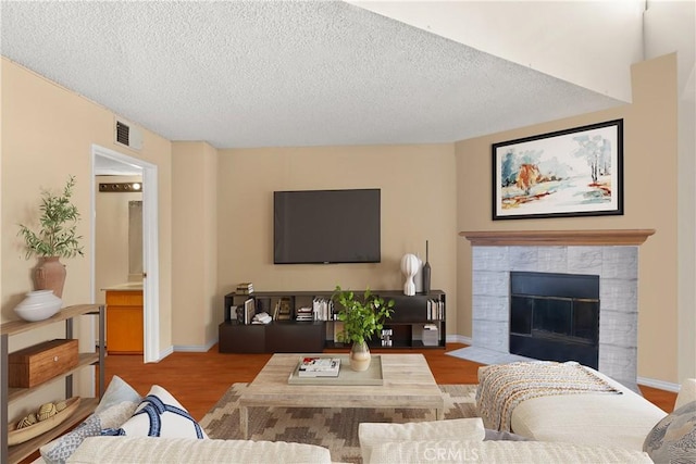 living room with light wood-type flooring, a textured ceiling, and a tile fireplace