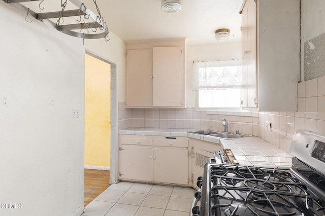 kitchen featuring stove, decorative backsplash, sink, light tile patterned flooring, and tile counters