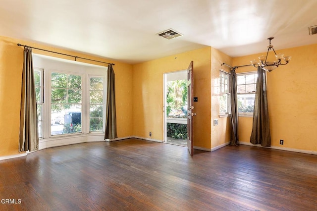 empty room featuring an inviting chandelier, plenty of natural light, and dark hardwood / wood-style floors