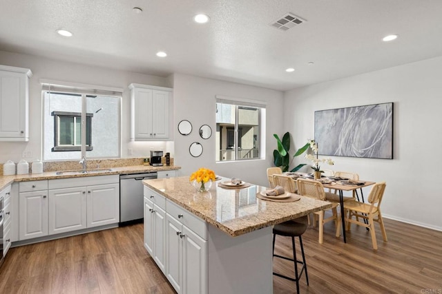 kitchen with dishwasher, a kitchen island, sink, hardwood / wood-style flooring, and white cabinets