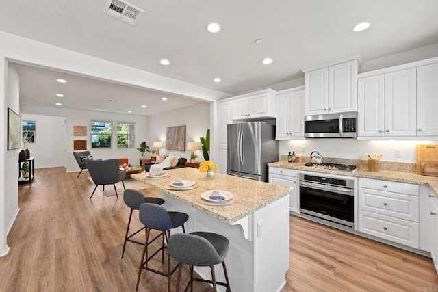 kitchen with light hardwood / wood-style floors, a breakfast bar, white cabinetry, appliances with stainless steel finishes, and light stone counters