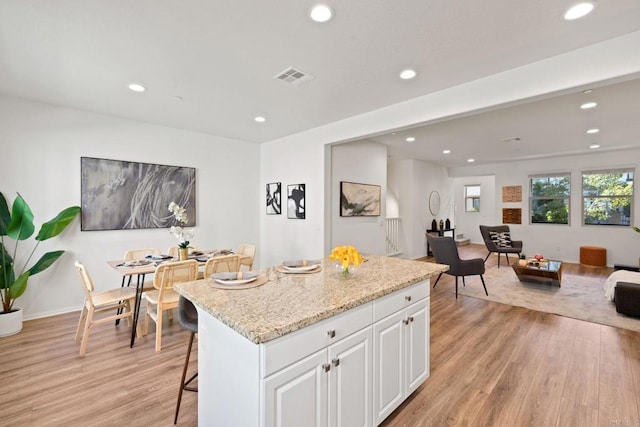 kitchen featuring light hardwood / wood-style floors, a center island, a breakfast bar, white cabinetry, and light stone countertops