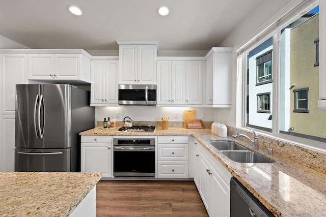 kitchen featuring white cabinets, appliances with stainless steel finishes, a healthy amount of sunlight, sink, and light stone counters