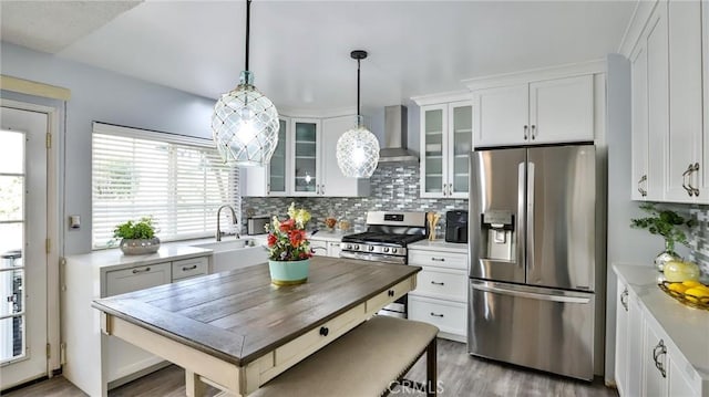 kitchen featuring pendant lighting, white cabinets, appliances with stainless steel finishes, wall chimney range hood, and sink