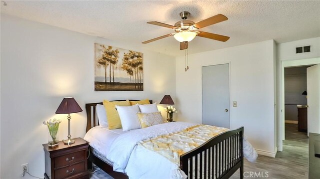 bedroom featuring ceiling fan, wood-type flooring, and a textured ceiling