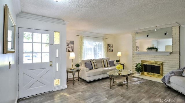 living room with hardwood / wood-style flooring, track lighting, a fireplace, a textured ceiling, and crown molding