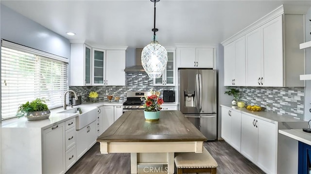 kitchen featuring sink, white cabinetry, hanging light fixtures, stainless steel appliances, and wall chimney exhaust hood