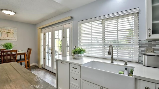 kitchen with tasteful backsplash, hardwood / wood-style floors, sink, white cabinetry, and french doors