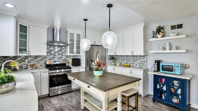 kitchen featuring decorative light fixtures, wall chimney range hood, sink, stainless steel appliances, and white cabinets