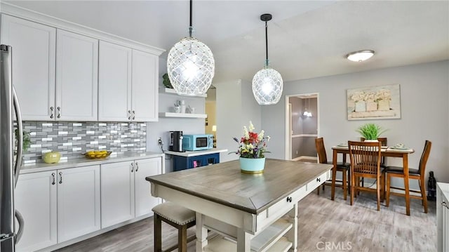 kitchen featuring light hardwood / wood-style floors, stainless steel fridge, decorative backsplash, hanging light fixtures, and white cabinets