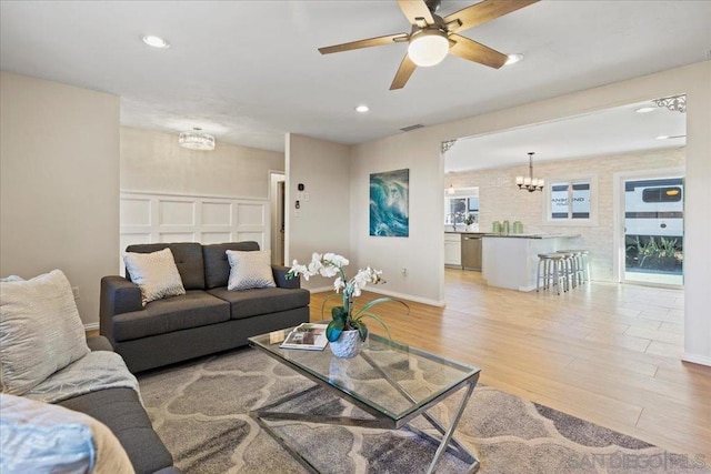 living room featuring ceiling fan with notable chandelier and light wood-type flooring