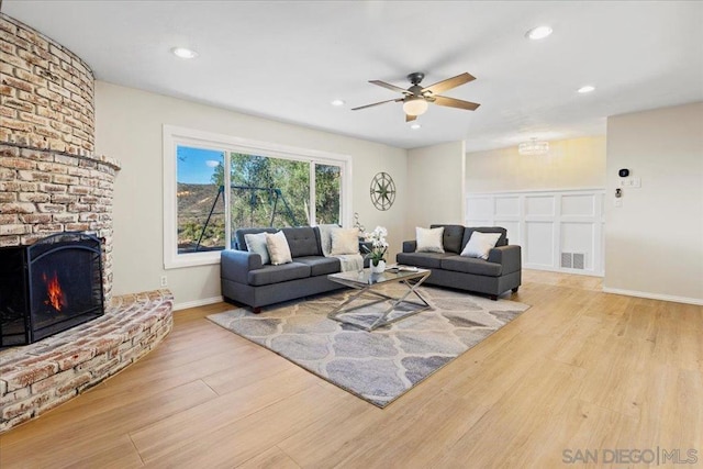 living room featuring a fireplace, light hardwood / wood-style floors, and ceiling fan