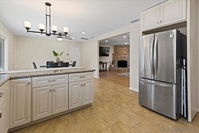 kitchen with ceiling fan with notable chandelier, white cabinetry, hanging light fixtures, stainless steel refrigerator, and a brick fireplace