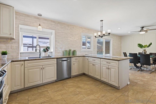 kitchen featuring ceiling fan with notable chandelier, pendant lighting, stainless steel appliances, sink, and light stone counters