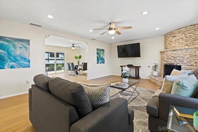 living room featuring ceiling fan, light hardwood / wood-style floors, and a fireplace