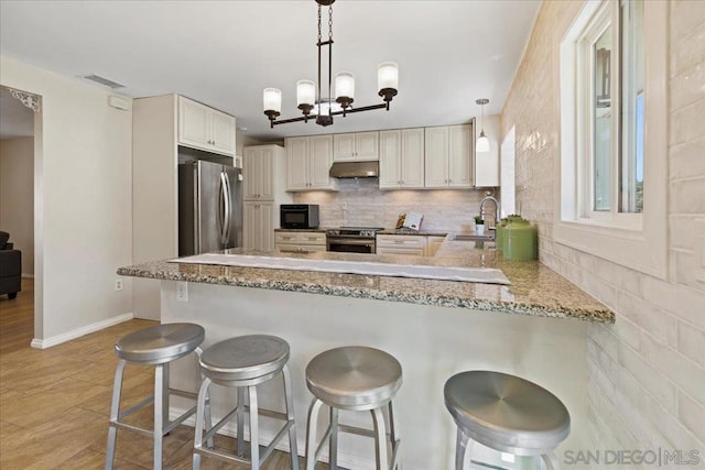 kitchen with decorative light fixtures, kitchen peninsula, appliances with stainless steel finishes, and a breakfast bar