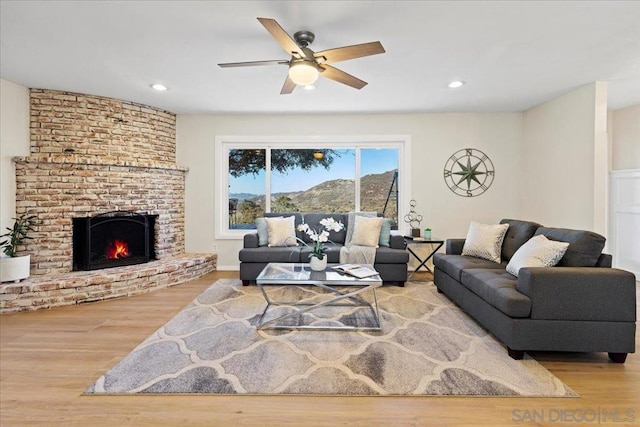 living room featuring ceiling fan, a fireplace, and light wood-type flooring