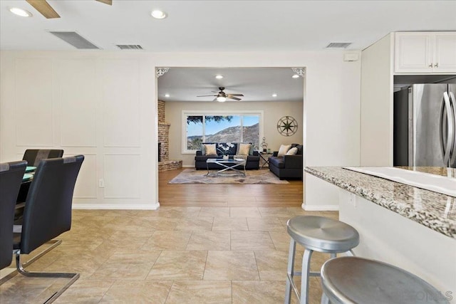 interior space with light stone countertops, a fireplace, stainless steel refrigerator, white cabinets, and ceiling fan