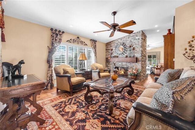 living room featuring hardwood / wood-style floors, a healthy amount of sunlight, a stone fireplace, and vaulted ceiling