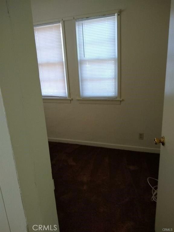 spare room featuring baseboards and dark colored carpet