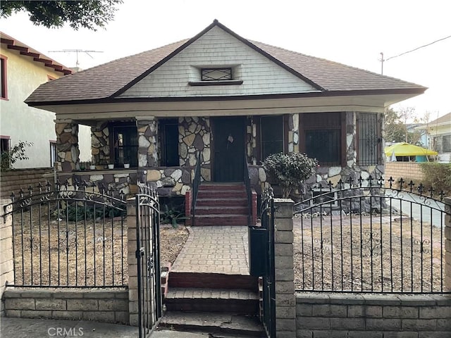 bungalow with a fenced front yard, a gate, a porch, and a shingled roof