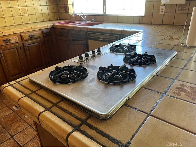 kitchen featuring white gas stovetop, a sink, tile counters, and decorative backsplash