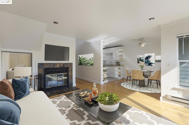 living room featuring ceiling fan, a tiled fireplace, crown molding, and hardwood / wood-style flooring