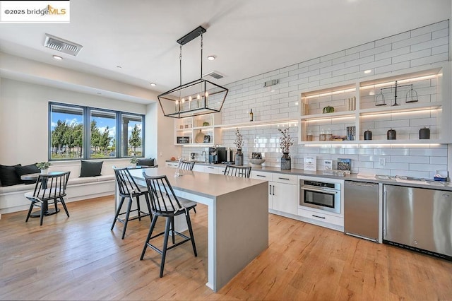 kitchen with a kitchen island, white cabinetry, hanging light fixtures, appliances with stainless steel finishes, and a kitchen breakfast bar