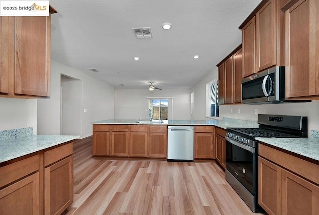 kitchen featuring ceiling fan, appliances with stainless steel finishes, light stone countertops, light hardwood / wood-style flooring, and sink