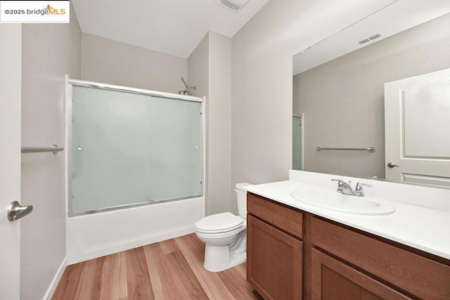 full bathroom with hardwood / wood-style floors, shower / bath combination with glass door, vanity, and toilet