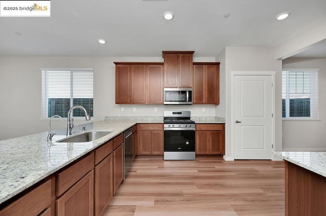 kitchen with light stone countertops, sink, appliances with stainless steel finishes, and light hardwood / wood-style flooring