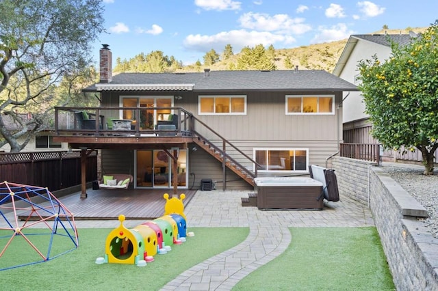 rear view of house featuring a playground, a deck, a hot tub, and a patio