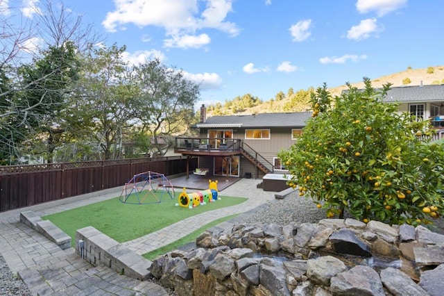 back of property featuring a playground, a patio area, a wooden deck, and a lawn