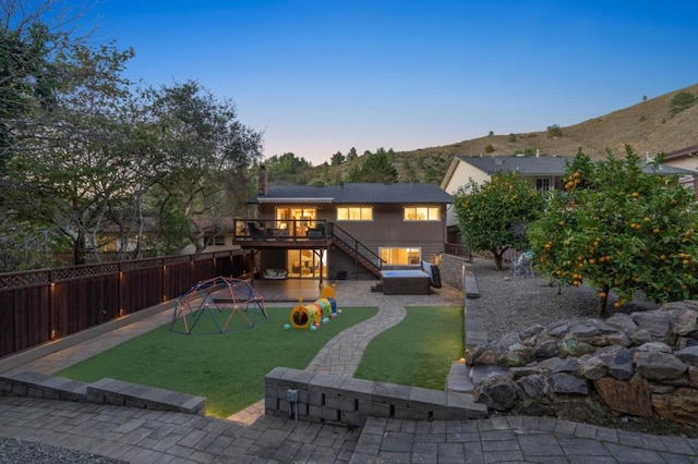 back house at dusk with a patio area, a playground, a lawn, and a deck with mountain view