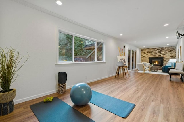 exercise room with a brick fireplace, crown molding, and light hardwood / wood-style floors