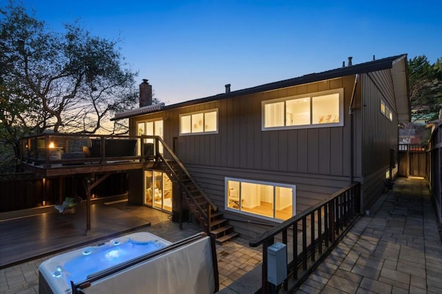 back house at dusk with a patio area, a deck, and an outdoor hot tub