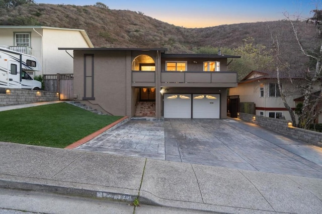 view of front facade with a yard, a garage, a mountain view, and a balcony