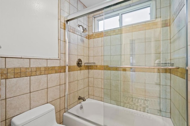 bathroom with toilet, bath / shower combo with glass door, and tile walls