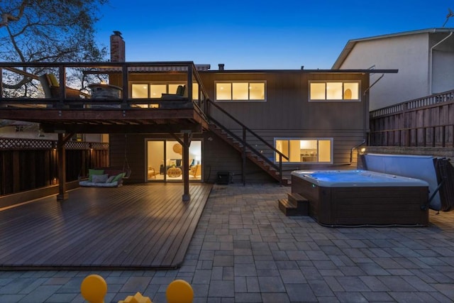 back house at dusk featuring a wooden deck, a hot tub, and a patio