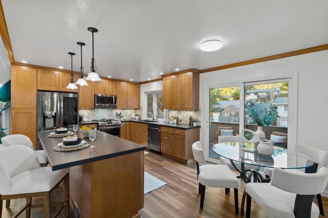 kitchen featuring decorative light fixtures, tasteful backsplash, light hardwood / wood-style floors, ornamental molding, and stainless steel appliances