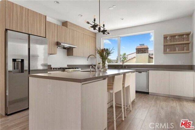 kitchen with appliances with stainless steel finishes, sink, a center island with sink, light hardwood / wood-style flooring, and a chandelier