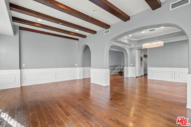 empty room featuring wood-type flooring, beamed ceiling, and an inviting chandelier